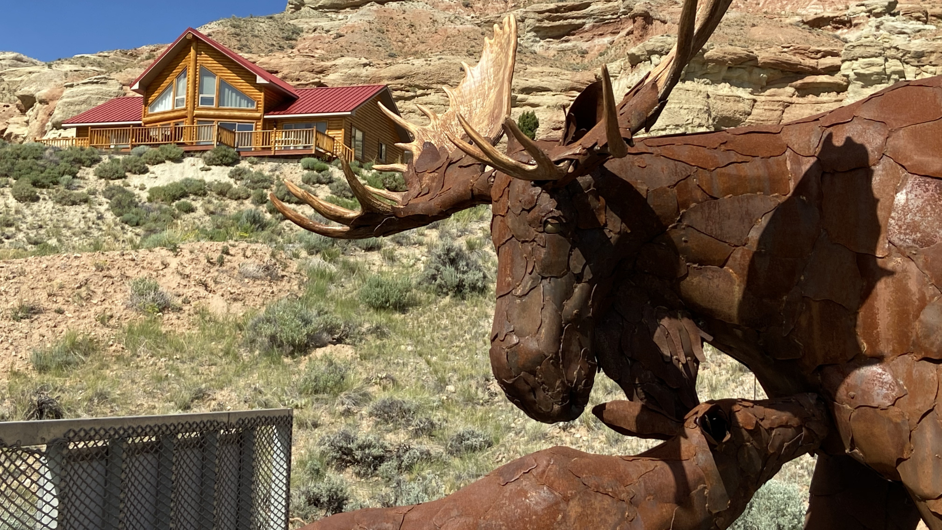 Steel moose sculpture photographed on the road during Carl Vanderheyden’s cross-country journey, stopped near a striking Western home